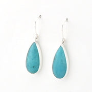 A pair of silver drop earrings featuring teardrop-shaped turquoise stones in silver bezel settings, suspended from silver fishhook wires on a plain white background.