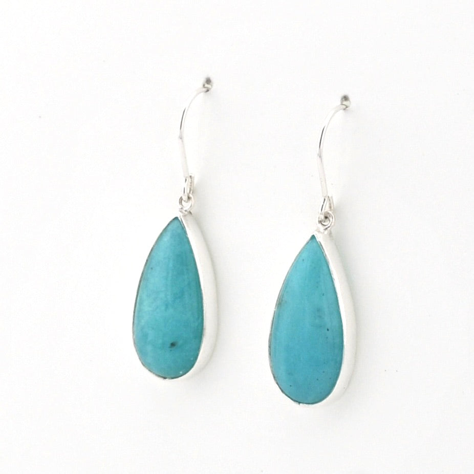 A pair of silver drop earrings featuring teardrop-shaped turquoise stones in silver bezel settings, suspended from silver fishhook wires on a plain white background.