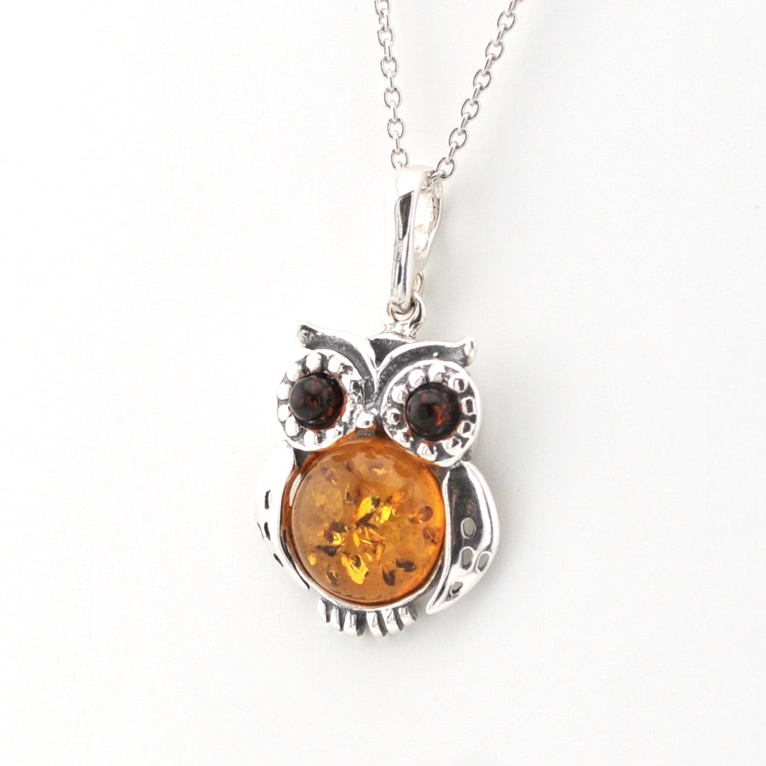 Silver owl pendant with amber center and brown stones on a white background