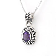A silver-toned oval pendant necklace featuring a central purple amethyst gemstone, detailed with textured scrollwork and rope-like borders, shown on a plain white background.