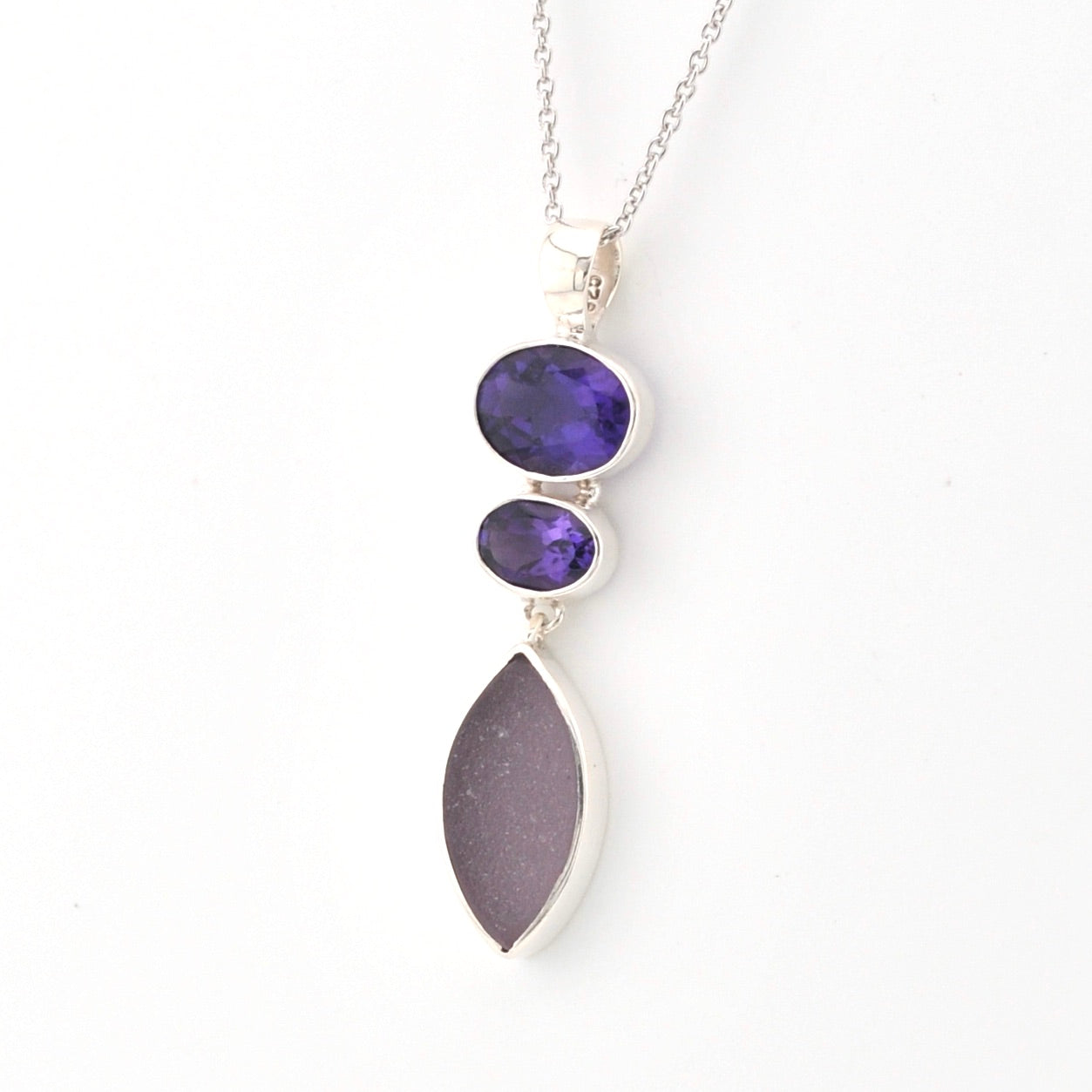 Necklace with purple gemstones and a marquise shaped piece of sea glass pendant on a white background