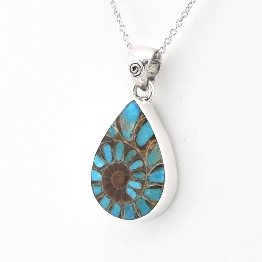 A silver teardrop pendant necklace featuring a natural ammonite fossil with a spiral pattern of turquoise blue and brown colors, suspended from a silver chain against a plain white background.