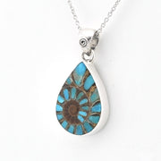 A silver teardrop pendant necklace featuring a natural ammonite fossil with a spiral pattern of turquoise blue and brown colors, suspended from a silver chain against a plain white background.