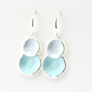 Pair of earrings with two circular discs, one silver and one light blue, on a white background.