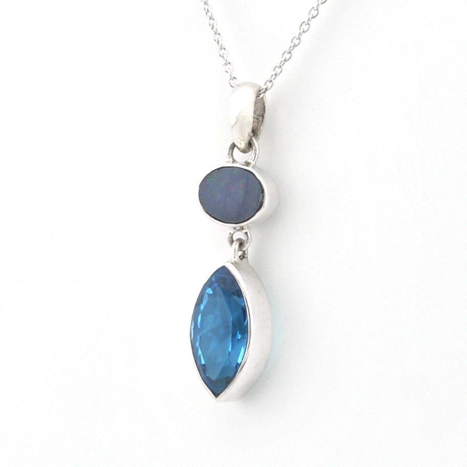 A silver pendant necklace featuring a marquise-cut blue gemstone and a smaller oval dark blue gemstone, shown on a plain white background.