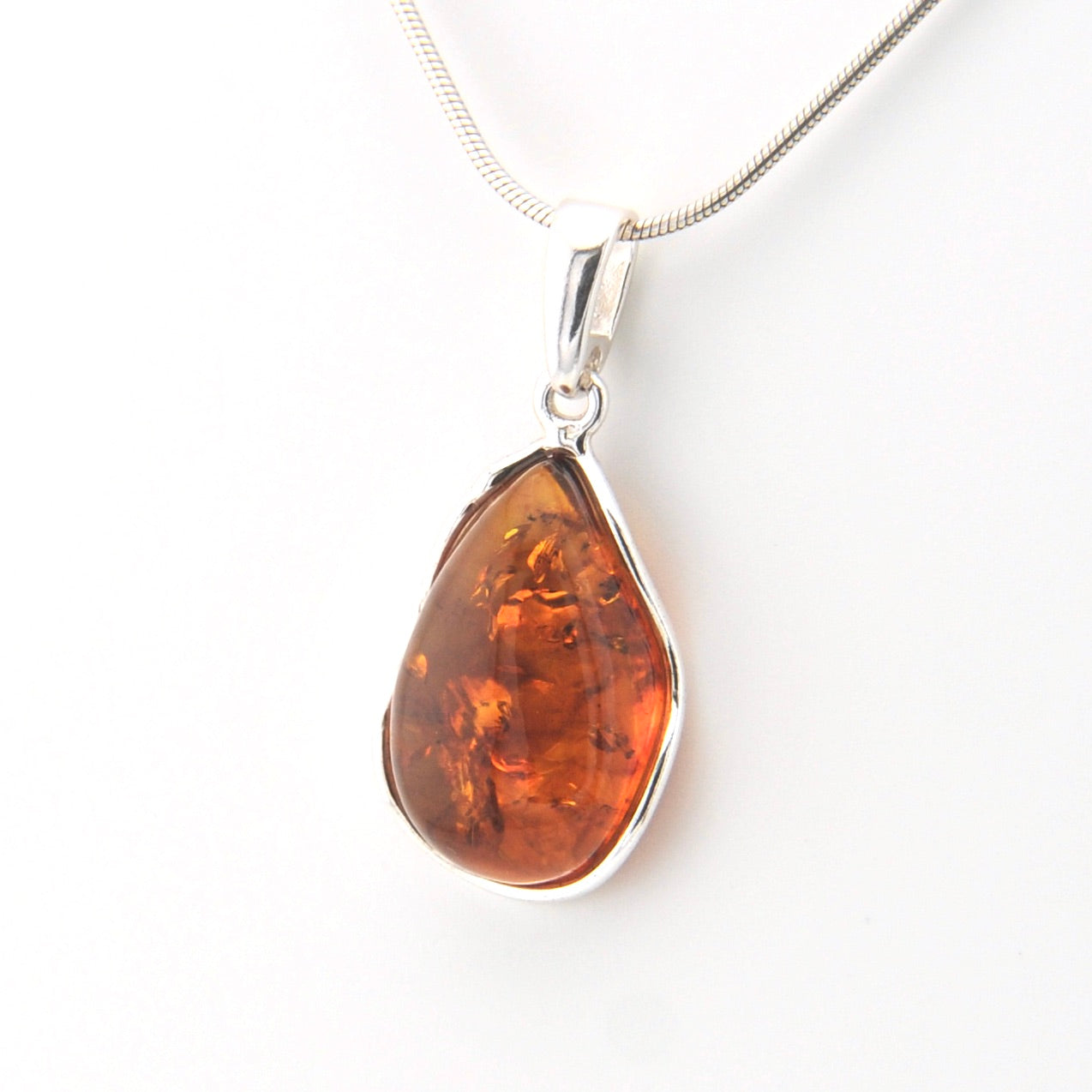 Teardrop-shaped amber pendant on a silver chain against a white background
