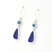 A pair of silver dangle earrings featuring a small round light blue gemstone and a larger teardrop-shaped deep blue sea glass shown on a plain white background.
