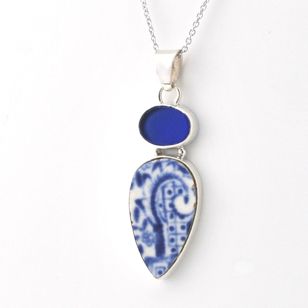 A silver pendant necklace featuring a teardrop-shaped blue and white patterned porcelain, a smaller round blue stone above it, and a silver chain against a plain white background.