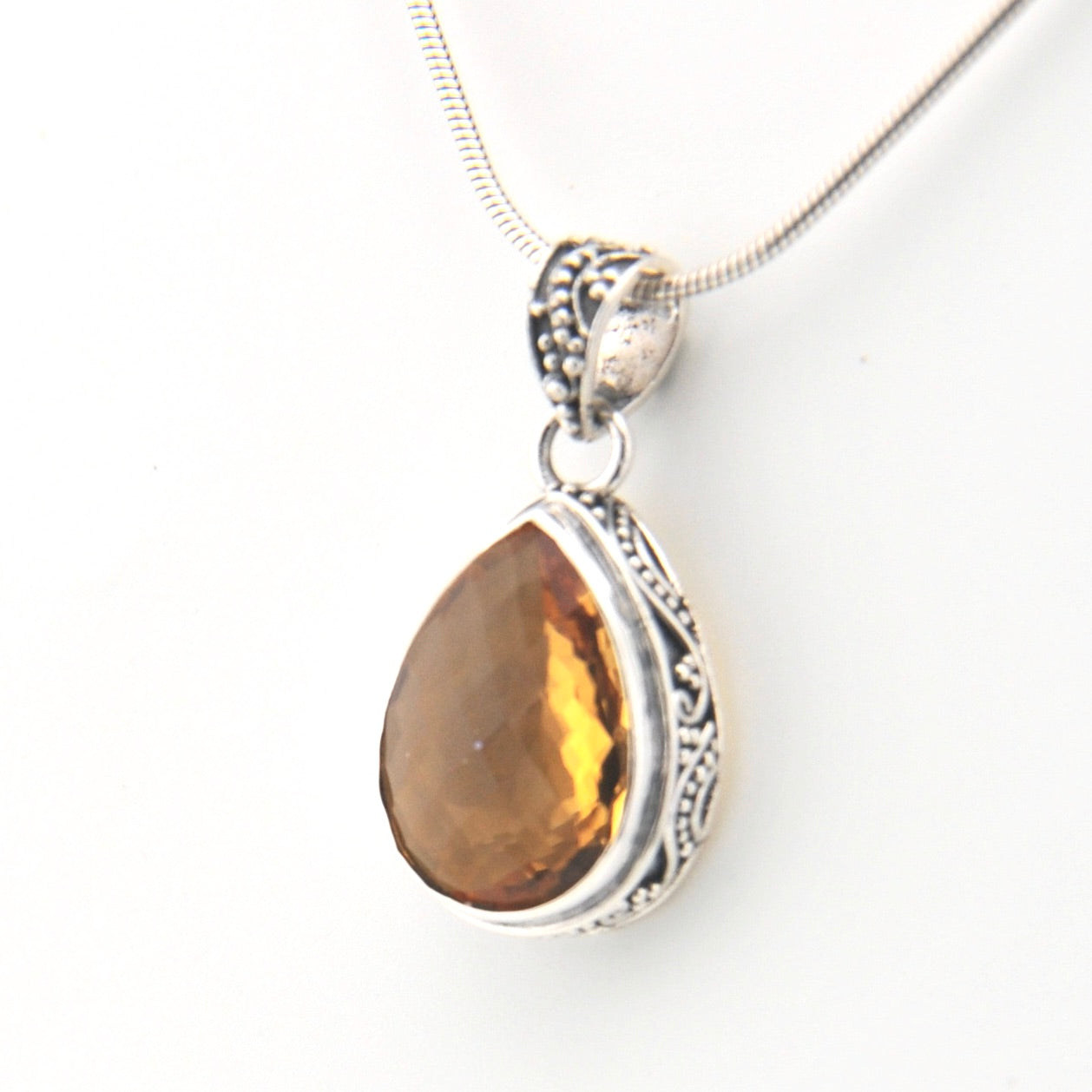 Teardrop-shaped citrine pendant on a silver chain against a white background