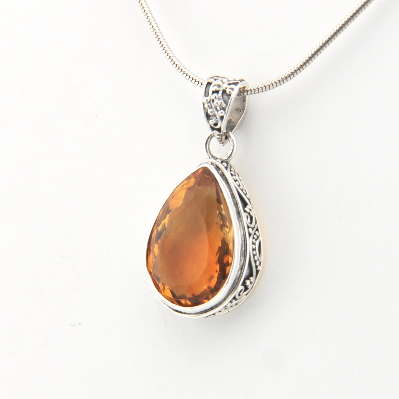 Teardrop-shaped citrine pendant on a silver chain against a white background