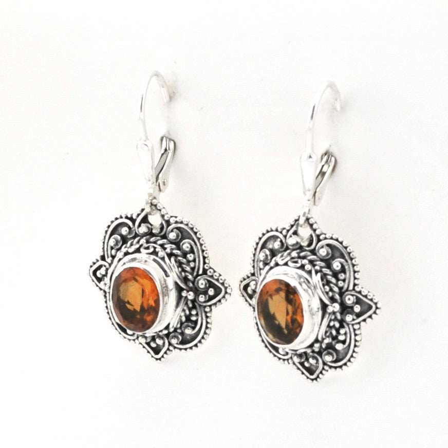 A pair of silver-toned dangle earrings with ornate filigree details and oval amber-colored gemstones, shown on a plain white background.