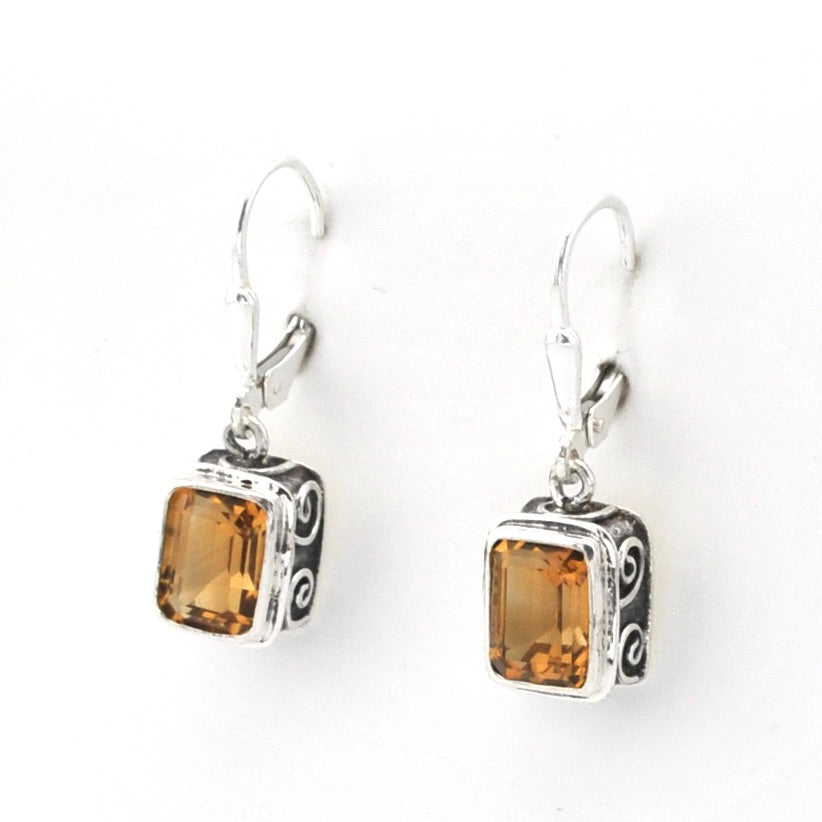 A pair of silver leverback earrings featuring rectangular amber-brown gemstones in ornate silver bezel settings, shown on a plain white background.