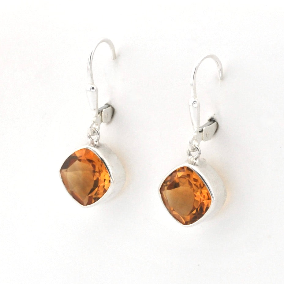 A pair of silver leverback earrings featuring faceted, cushion-cut amber-orange gemstones in silver bezel settings, shown on a plain white background.