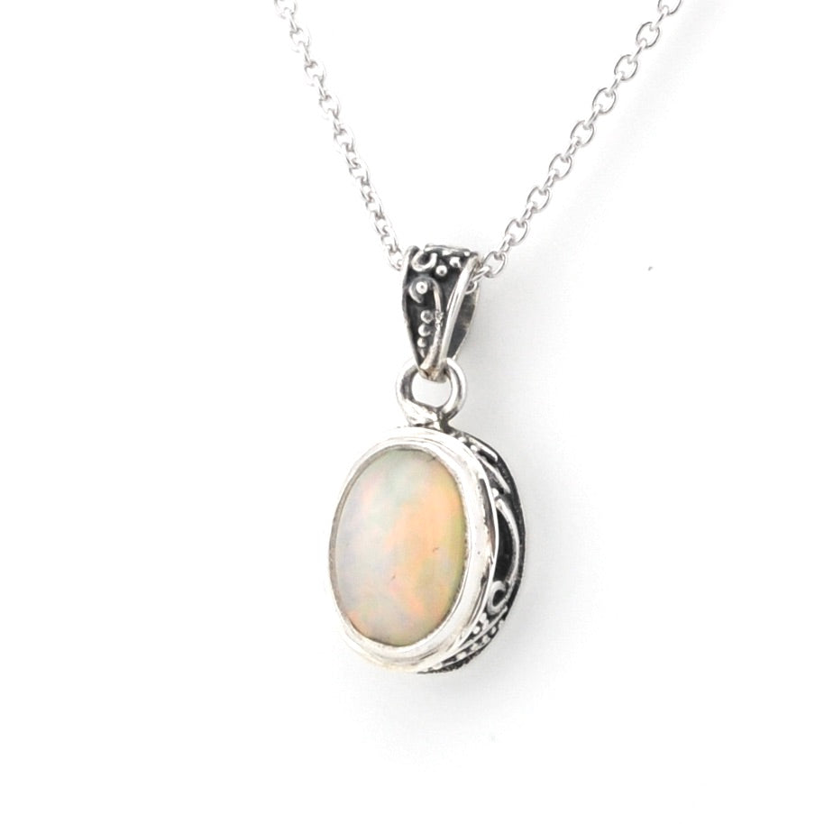 A silver pendant necklace featuring an oval cabochon opal gemstone with iridescent colors, set in an ornate silver bezel on a delicate silver chain.