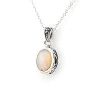 A silver pendant necklace featuring an oval cabochon opal gemstone with iridescent colors, set in an ornate silver bezel on a delicate silver chain.