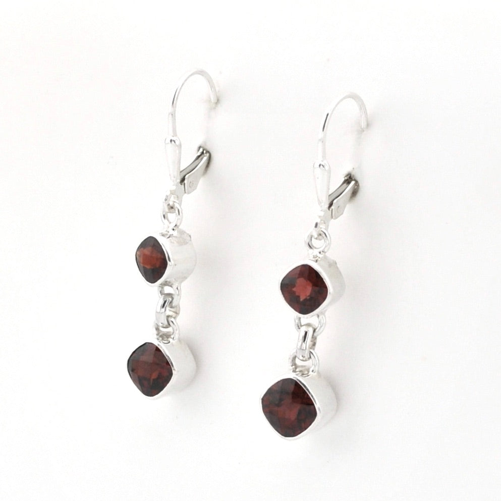 A pair of silver leverback dangle earrings featuring two small square bezel-set dark red garnet stones, shown against a plain white background.