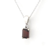 A silver pendant necklace featuring a rectangular dark red garnet gemstone in a four-prong setting, suspended from a delicate silver chain against a plain white background.