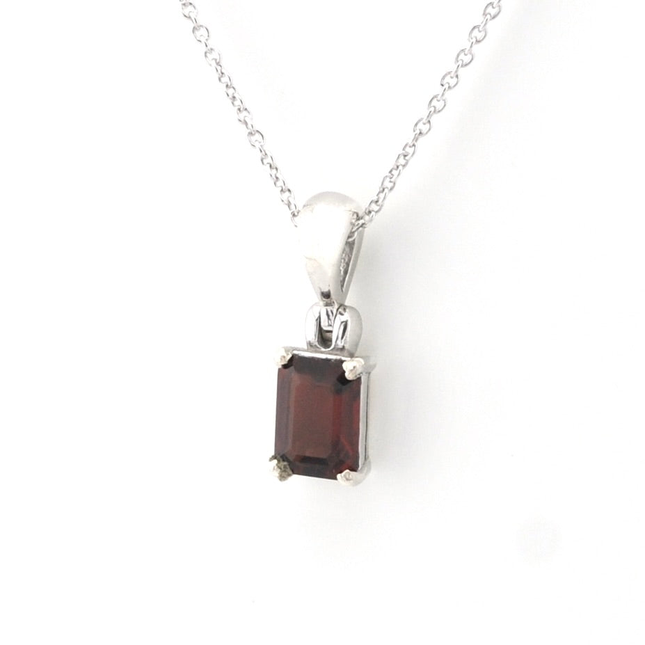 A silver pendant necklace featuring a rectangular dark red garnet gemstone in a four-prong setting, suspended from a delicate silver chain against a plain white background.