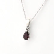 A silver pendant necklace featuring a teardrop-shaped dark red gemstone, displayed on a clean white background.