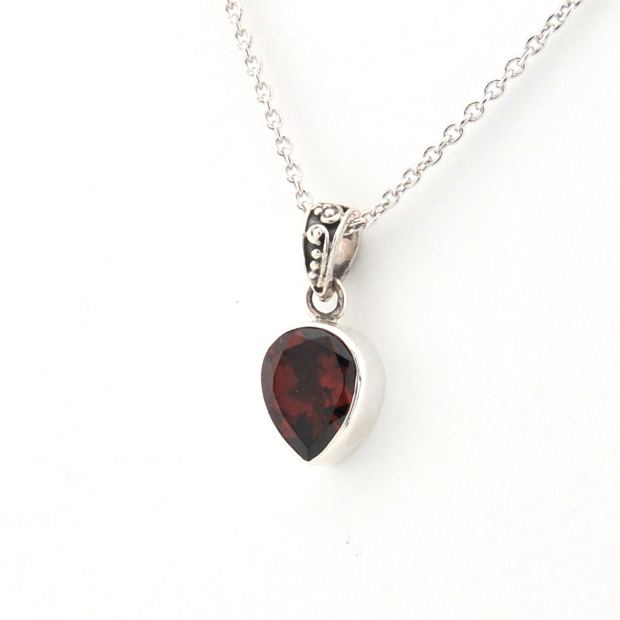 Silver necklace with a teardrop-shaped garnet pendant on a white background
