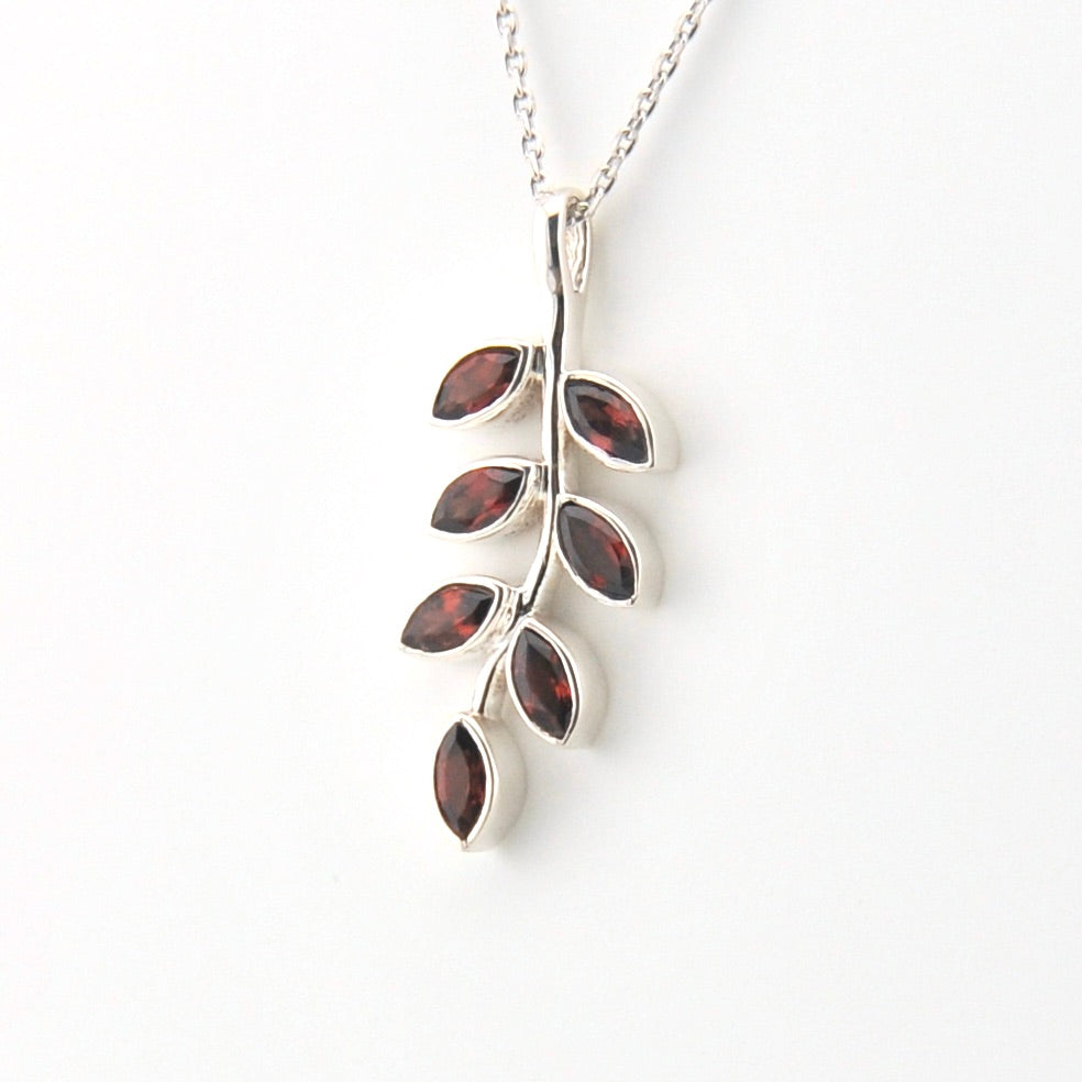 Silver necklace with a leaf-shaped pendant featuring red stones on a white background