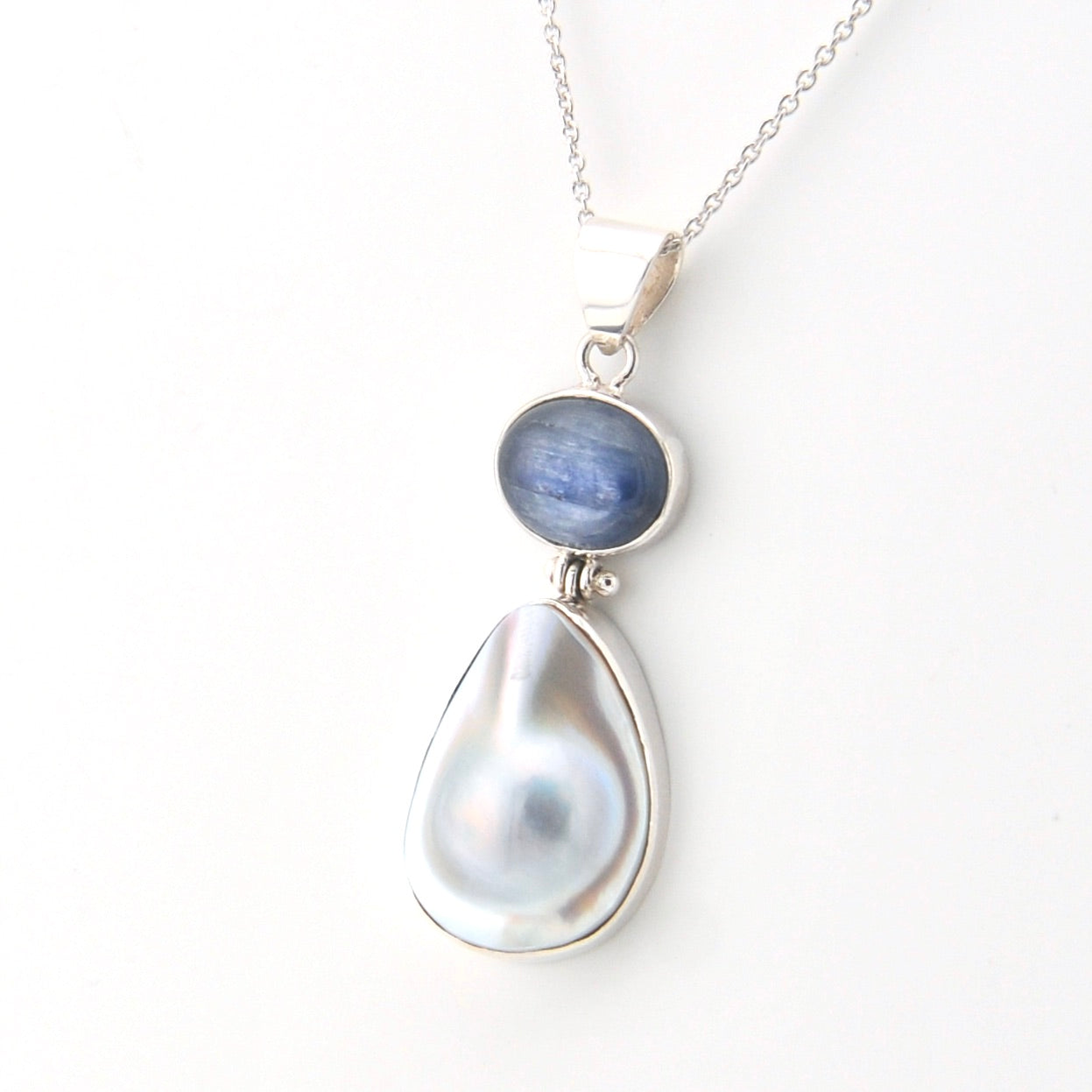 Necklace with a teardrop-shaped pearl and blue gemstone on a white background