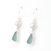 A pair of silver drop earrings featuring a small white pearl and a teardrop-shaped sea glass charm in a muted sage green color, set against a plain white background.