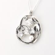 Silver pendant with floral design and pearls on a white background