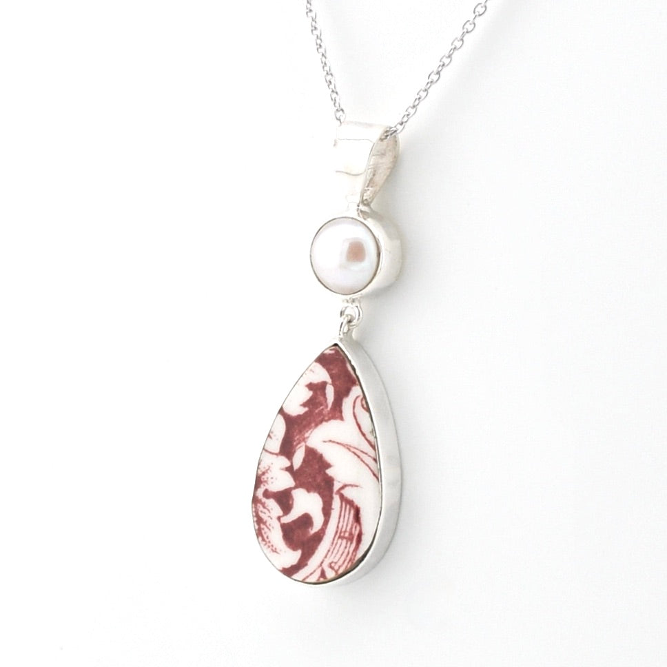 A silver pendant necklace featuring a teardrop-shaped marbled stone with brown and white swirls, a round white pearl, and a silver chain on a white background.