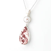 A silver pendant necklace featuring a teardrop-shaped marbled stone with brown and white swirls, a round white pearl, and a silver chain on a white background.