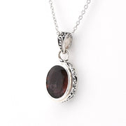 A silver chain necklace with an oval pendant featuring a dark reddish-brown gemstone in an ornate silver bezel setting, shown against a plain white background.