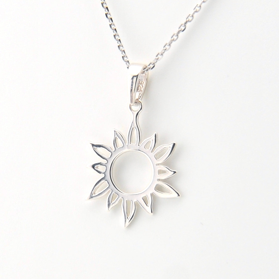 Silver sun-shaped pendant necklace on a white background