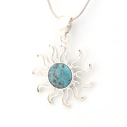 Silver sun-shaped pendant with a turquoise center on a white background