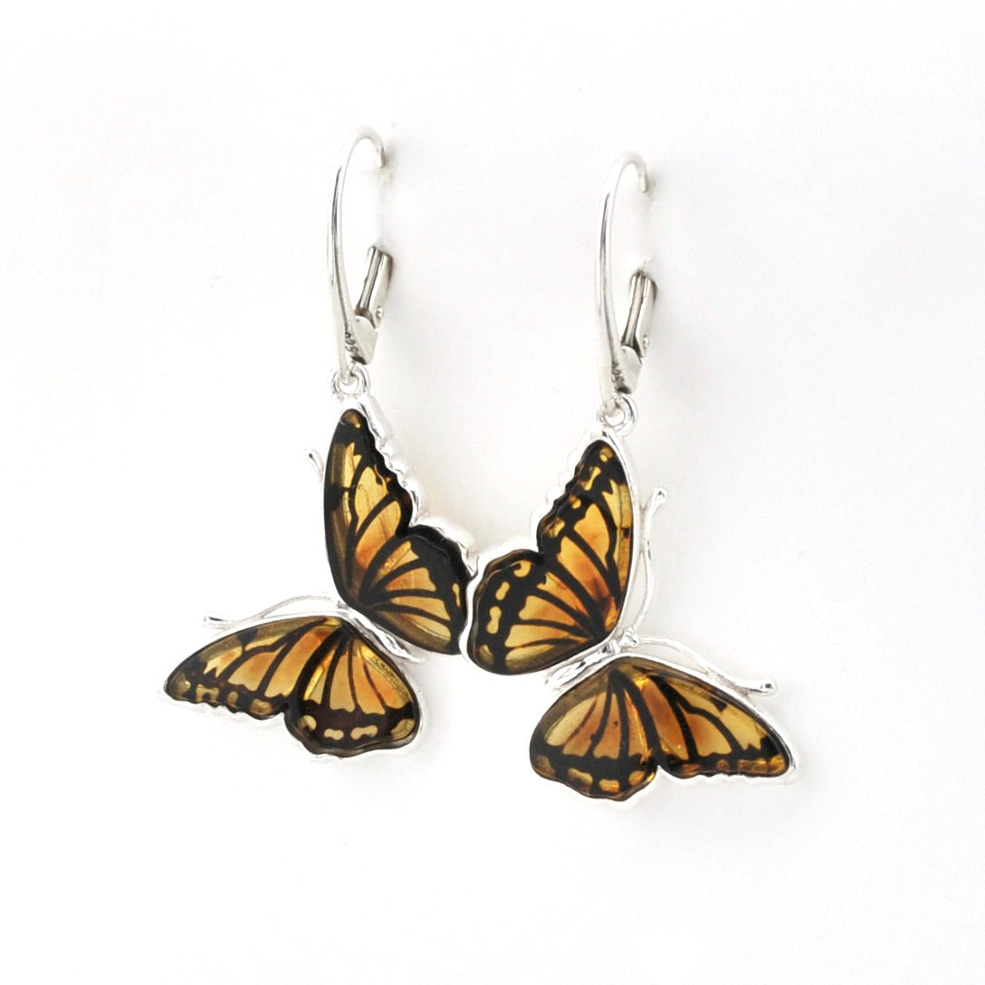 A pair of silver leverback earrings featuring butterfly wings with orange, yellow, and black patterned enamel, shown on a plain white background.