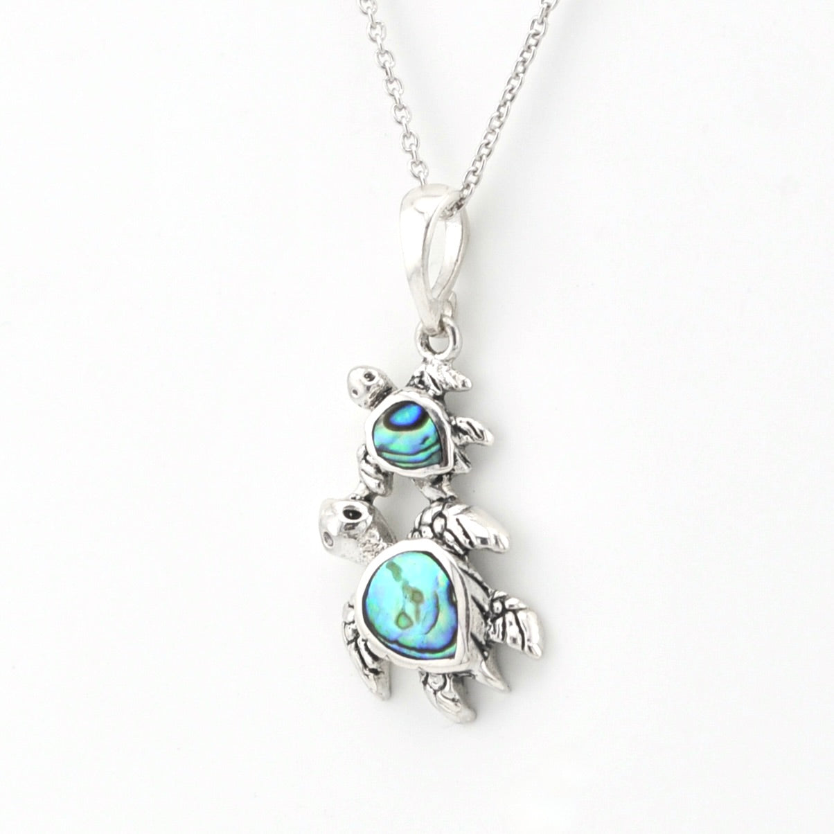A sterling silver pendant necklace featuring a mother-and-child turtle design, detailed with iridescent blue abalone shell inlays on the turtle shells, shown on a white background.