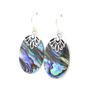 A pair of dangle earrings featuring oval abalone shell with iridescent blue, green, and black patterns, suspended from silver filigree caps and silver fishhook wires, shown against a plain white background.