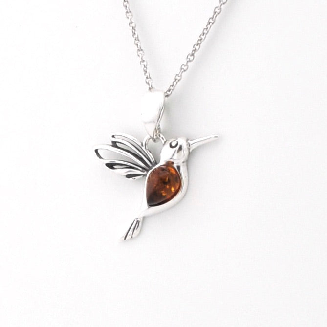 A sterling silver hummingbird pendant necklace with a polished amber-brown heart-shaped gemstone, shown on a clean white background.
