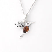 A sterling silver hummingbird pendant necklace with a polished amber-brown heart-shaped gemstone, shown on a clean white background.