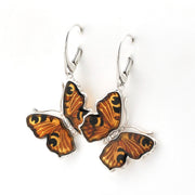 A pair of butterfly-shaped dangle earrings with orange and black patterned wings set in silver-tone metal hooks, shown on a plain white background.