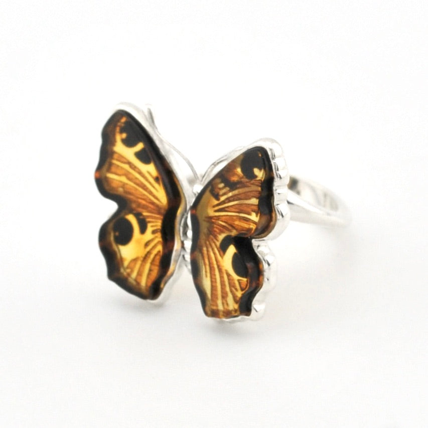 A silver butterfly ring featuring detailed amber and black patterned wings, set against a plain white background.
