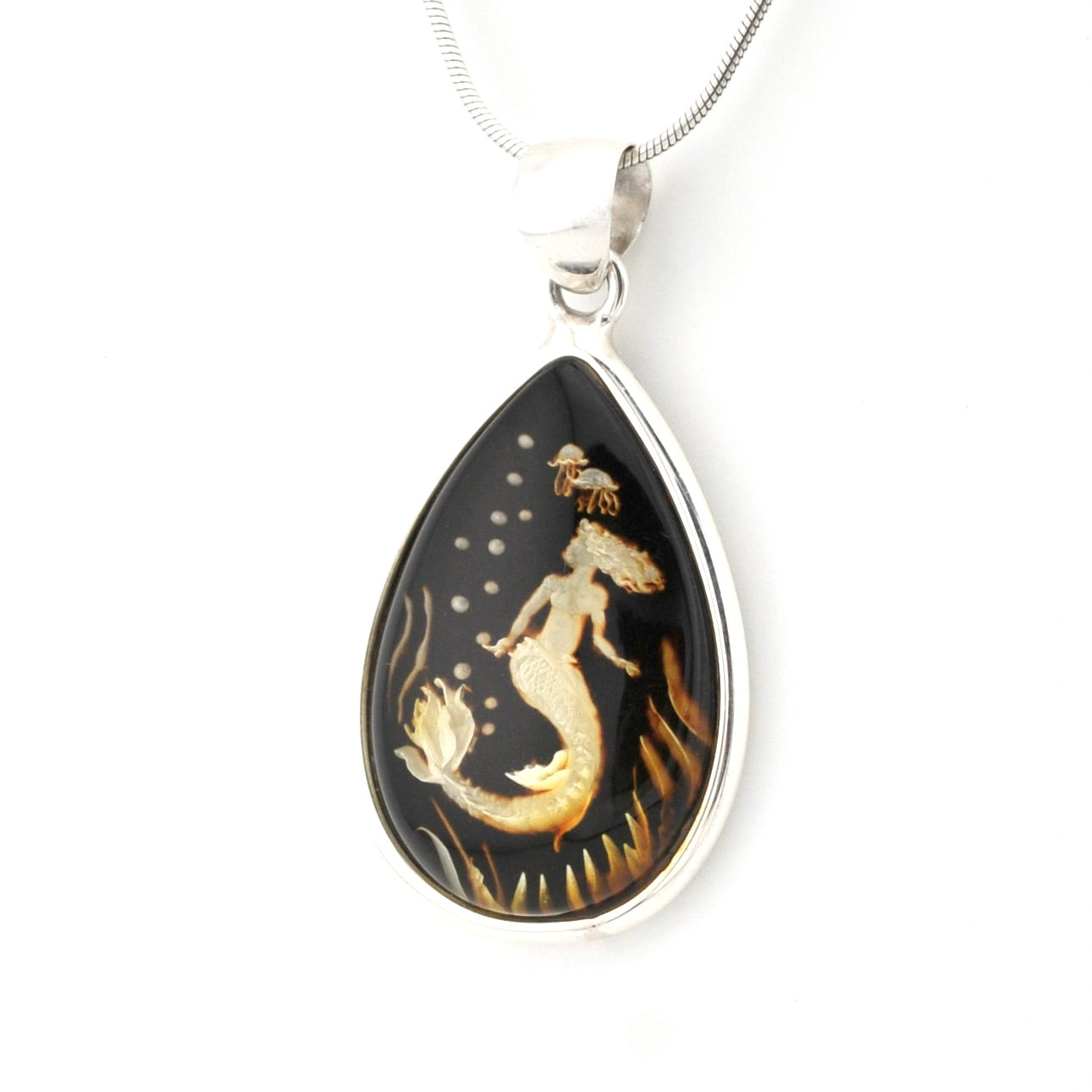 A teardrop-shaped pendant necklace featuring a mermaid design on a black background with gold and white details, set in a silver-tone frame and suspended from a silver chain.