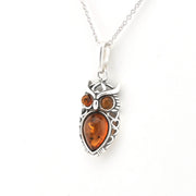 A silver owl pendant necklace featuring a large teardrop-shaped amber gemstone in the center and two smaller round amber stones for the eyes, suspended from a silver chain against a plain white background.
