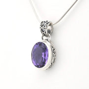 A silver pendant necklace featuring an oval-cut purple gemstone in an ornate silver bezel setting, suspended from a silver snake chain against a plain white background.
