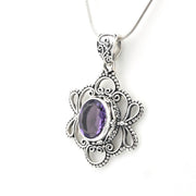 An ornate silver pendant necklace featuring a central oval purple gemstone surrounded by detailed filigree and beaded silver borders, suspended from a silver chain against a plain white background.
