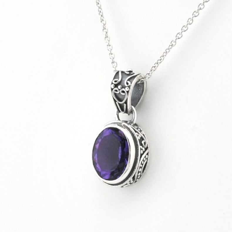 A silver pendant necklace featuring an oval purple gemstone in an ornate silver bezel setting, suspended from a delicate silver chain against a plain white background.