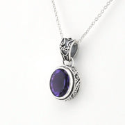 A silver pendant necklace featuring an oval purple gemstone in an ornate silver bezel setting, suspended from a delicate silver chain against a plain white background.
