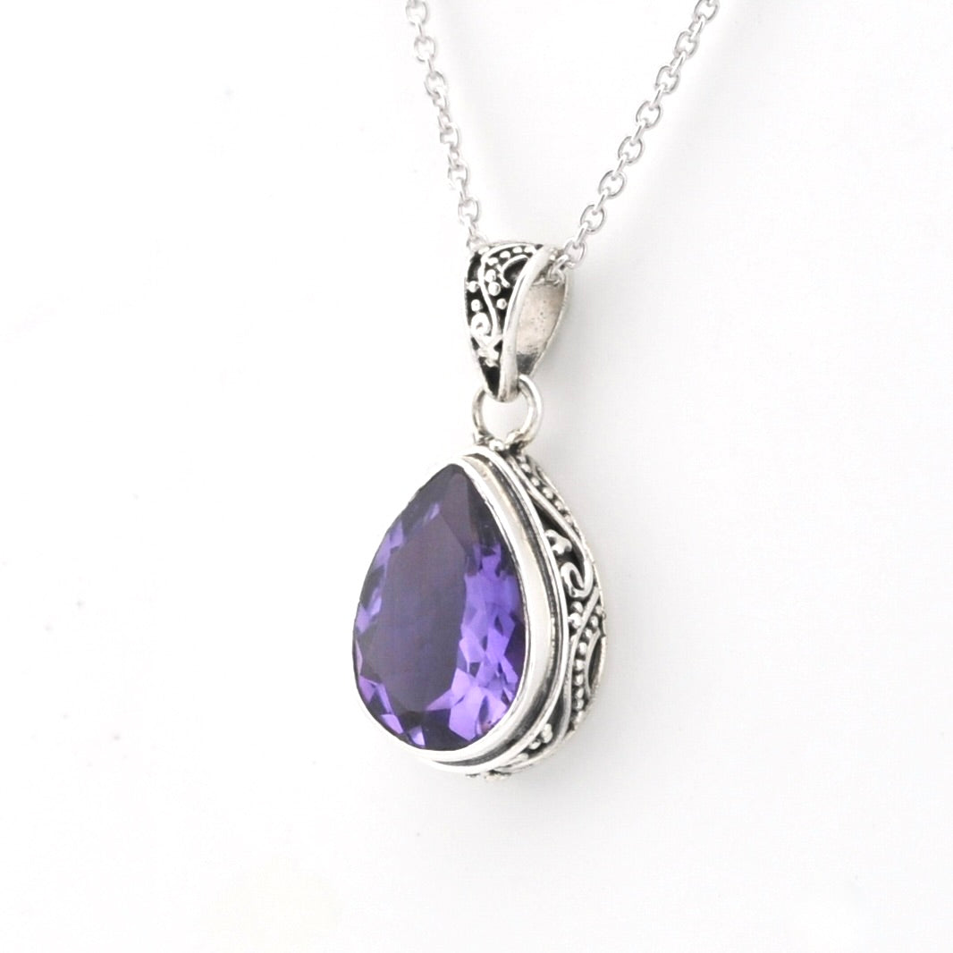 A silver teardrop pendant necklace featuring a faceted purple gemstone, set in an ornate silver bezel with a delicate silver chain against a plain white background.