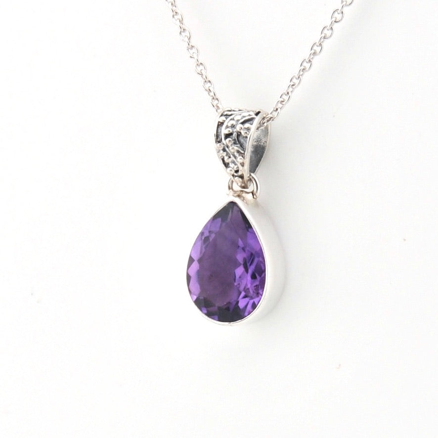 A silver teardrop pendant necklace featuring a faceted purple gemstone, suspended from a delicate silver chain against a plain white background.