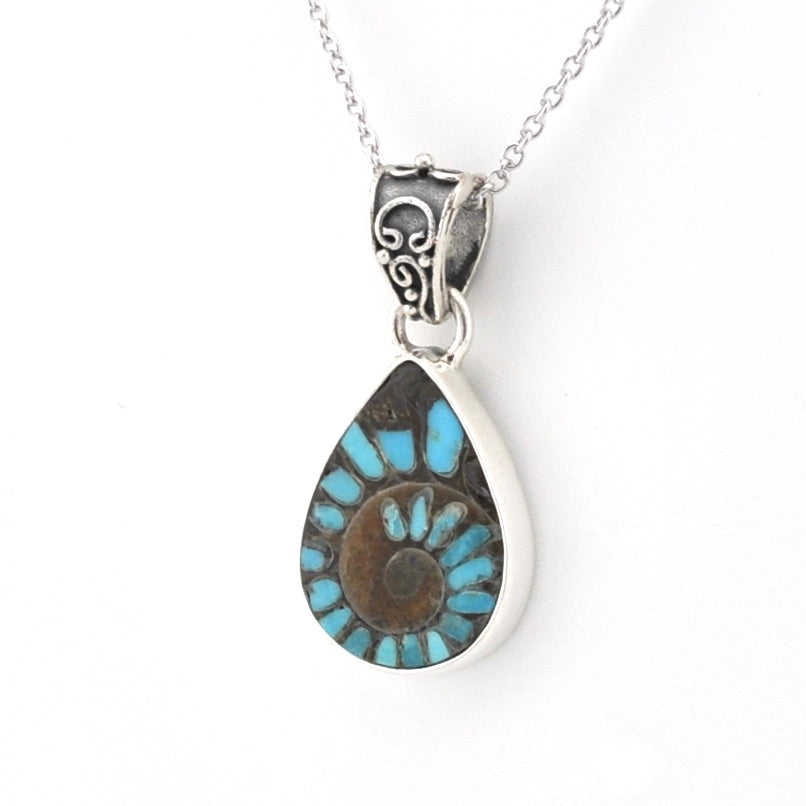 A teardrop-shaped pendant necklace featuring a natural brown and turquoise ammonite shell pattern set in a silver-tone bezel, suspended from a silver chain on a white background.