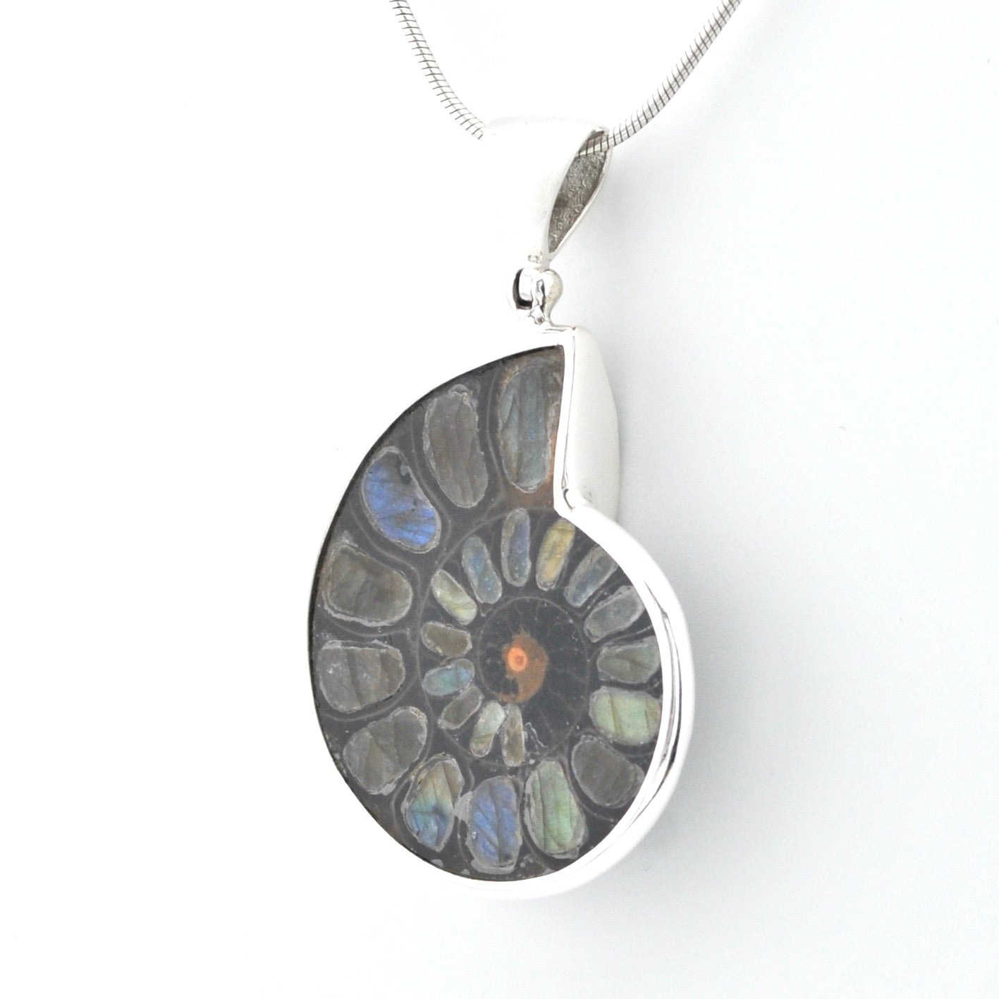 A silver pendant necklace featuring a polished ammolite shell-shaped stone with a spiral pattern of gray, blue, and green iridescent inclusions, suspended from a silver chain against a white background.